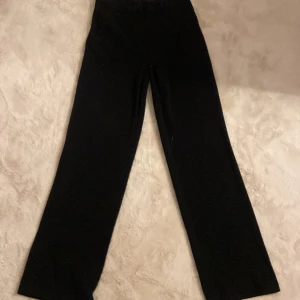 Svarta kostymbyxor från Vero Moda - Svarta kostymbyxor från Vero Moda med klassisk rak passform och hög midja. Byxorna har vida ben och är tillverkade i ett mjukt tyg som ger en snygg siluett. Perfekta att styla med sneakers eller boots för en clean look.