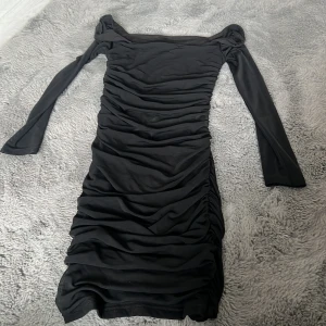 Svart långärmad klänning från SHEIN - Snygg svart långärmad klänning från SHEIN med rynkade detaljer längs hela klänningen. Den har en tight passform och fyrkantig urringning, perfekt för dig som vill ha en stilren och trendig look.