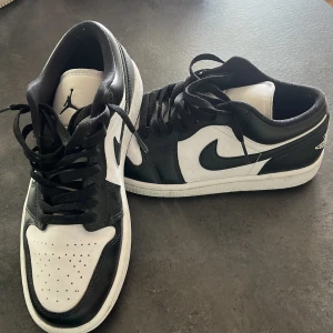 Nike Air Jordan 1 Low svart/vit - Snygga Nike Air Jordan 1 Low sneakers i svart och vitt skinn med klassisk swoosh på sidan och Jordan-logga på tungan. Lågt skaft och snörning ger en clean och sportig look som passar till det mesta.