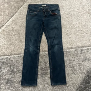 Mörkblå jeans från Lee Women - Snygga mörkblå jeans från Lee Women med klassisk femficksdesign och raka ben. Jeansen har orange kontrastsömmar, dubbla knappar i midjan och är tillverkade i slitstarkt denim. Perfekta för dig som gillar en tidlös och clean look.