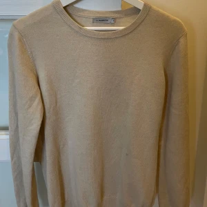 Beige stickad tröja från J.Lindeberg - En stilren beige stickad tröja från J.Lindeberg med rund halsringning och ribbade muddar. Perfekt för lager-på-lager och funkar lika bra till jeans som till chinos. Enkel och klassisk design som passar till många olika looks.