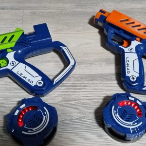 LZMAD - Bilden visar två leksakspistoler och två elektroniska sensorer, troligen för laserspel. Det finns ingen bok synlig på bilden.