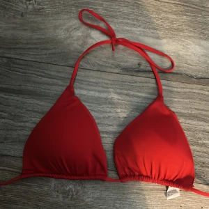 Röd trekantsbikini med knyt - Snygg röd trekantsbikini med knyt i nacken och under bysten. Klassisk modell som är perfekt för stranden eller poolen. Enkel och stilren design som ger en fräsch look hela sommaren. Vadderade kupor