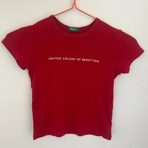 Baby tee från United Colors of Benetton - Ålder 5-6. Röd t-shirt från United Colors of Benetton med vit text på bröstet. Klassisk rund halsringning och korta ärmar. Tillverkad i mjuk bomull som känns skön mot huden. Enkel och stilren design som passar perfekt till jeans eller shorts. 