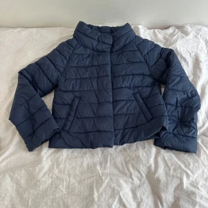 Mörkblå pufferjacka från Gina Tricot - Snygg mörkblå pufferjacka från Gina Tricot med quiltad design och hög krage. Jackan har långa ärmar och två snedställda fickor framtill. Perfekt för kyliga dagar när du vill hålla stilen enkel och clean.🤩 säljer på grund av att jag köpte en för liten storlek. kan sänka pris vid snabb affär!!!