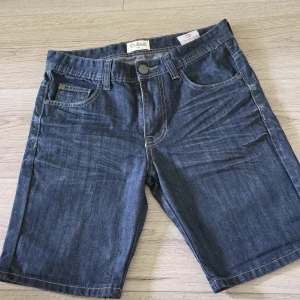 Mörkblå jeansshorts från Cubus - Klassiska mörkblå jeansshorts från Cubus. Modellen är rak och slutar strax ovanför knäna. .
