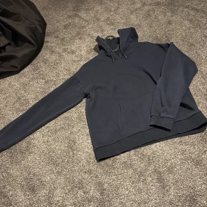 Mörkblå hoodie från Gina Tricot - Mörkblå hoodie från Gina Tricot med klassisk känguruficka och snörning i huvan. Tröjan har ribbade muddar och är tillverkad i mjuk bomullsmix. Perfekt för en chill och avslappnad stil.