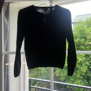 Svart kofta från Mango med knappar - En klassisk svart kofta från Mango med rund halsringning och silverfärgade knappar framtill. Långärmad och i mjukt stickat material som passar perfekt till lager-på-lager. Enkel och stilren design som funkar till det mesta.