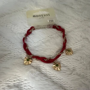 Rött armband med hjärta - Snyggt armband med röd flätad textil och guldfärgad kedja. Tre hjärta med grön sten ger en unik touch. Perfekt accessoar för att lyfta din stil med lite färg och detaljer.