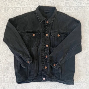 Svart jeansjacka från Monki - Säljer en svart jeansjacka från Monki i storlek S. Klassisk modell med bronsfärgade knappar framtill och på bröstfickorna. Jackan har krage, långa ärmar och två sidofickor. Perfekt för en cool och avslappnad stil.