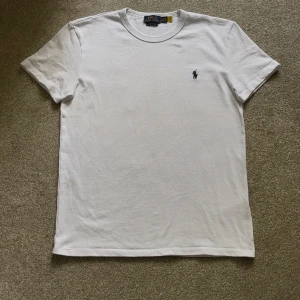 Vit t-shirt från Polo Ralph Lauren - Klassisk vit t-shirt från Polo Ralph Lauren med broderad marinblå logga på bröstet. Modellen är kortärmad och har en rund halsringning. Tillverkad i mjuk bomull och har en clean, stilren look som funkar till allt. Skick: 10/10, Storlek S.