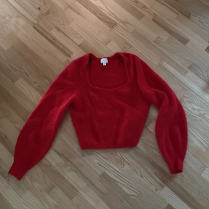 Röd croppad stickad tröja - Trendig röd stickad tröja med croppad passform och fyrkantig urringning. Långa ärmar med lätt puff och ribbad struktur ger en snygg siluett. Perfekt för dig som vill sticka ut med färg och stil.