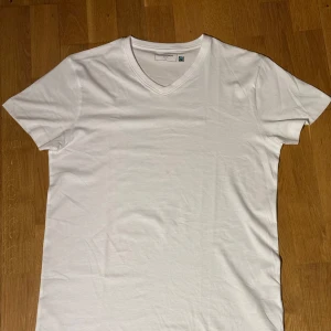 Vit v-ringad t-shirt i bomull - Klassisk vit t-shirt från Neutral med v-ringning och korta ärmar. Tillverkad i mjuk bomull som känns skön mot huden. Enkel och stilren design som passar till det mesta. Perfekt basplagg för garderoben.