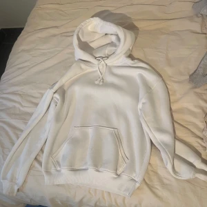 Vit hoodie med huva och ficka - Säljer en klassisk vit hoodie med huva och dragsko från bikbok. Tröjan har en stor magficka och ribbade muddar vid ärmslut och nederkant. Perfekt för en chill och avslappnad stil.