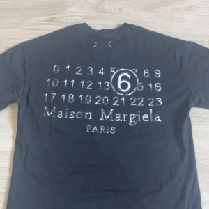 Maison Margiela svart t-shirt - Svart t-shirt från Maison Margiela med ikoniskt siffror-tryck och stor 6:a på ryggen. Klassisk passform, rund hals och korta ärmar. Tillverkad i mjuk bomull och har de typiska vita sömmarna på ryggen. Perfekt för dig som gillar streetstyle och designerplagg.helt oanvänd endast testad,säljer pga för stor ,size s men är oversized 