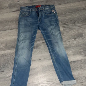 Blå Replay jeans med tvättad look - Säljer ett par blå jeans från Replay med snyggt tvättad effekt och klassiska fem fickor. Jeansen har normal passform och raka ben, med detaljer som synliga sömmar och Replay-logga på bakfickan. Perfekta för en avslappnad stil.