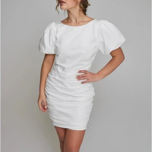 Vit kort klänning med puffärm -  Vit kortklänning med puffiga ärmar och rynkade detaljer längs sidorna. Klänningen har en öppen rygg och en figurnära passform. Den har lapparna kvar och är oanvänd💞