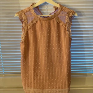 Rosa blus med spets  - Supersöt rosa blus från SHEIN i storlek XS. Blusen har ärmlös design, spetsdetaljer vid axlar och hals, samt små broderade prickar över hela tyget. Tillverkad i lätt polyester, perfekt för vår och sommar. Ger en och trendig vibe!
