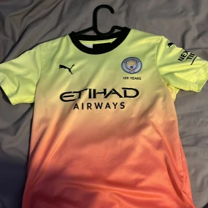 Manchester City Sterling 7 Puma tröja sterling - Manchester City fotbollströja från Puma med Sterling 7 på ryggen. Tröjan har en snygg färgövergång från gul upptill till orange nedtill, svart krage och tryckta loggor. Materialet är lätt och andas, perfekt för fotbollsträning eller match.