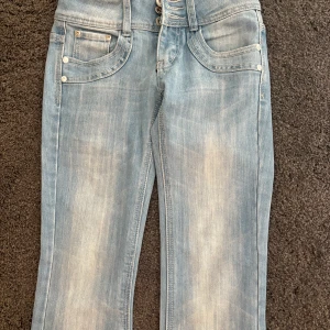 Ljusblå jeans från Revers Jeans - Snygga ljusblå jeans från Revers Jeans med snygga fickor och tydliga slitningar för en cool, avslappnad look. Jeansen är flare/ lite raka och silverfärgade nitar samt knappar framtill. Lågmidjade. Pris kan diskuteras vid snabb affär 