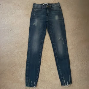 Blå skinny jeans från Zara med slitningar - Snygga blå skinny jeans från Zara med slitna detaljer och fransade benslut. Jeansen har klassisk femficksdesign, dragkedja och knapp framtill. Perfekta för dig som gillar en trendig och avslappnad look.