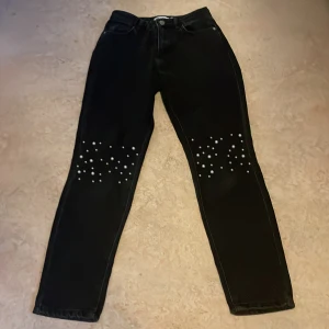 Svarta jeans med pärldetaljer från NA-KD - Svarta jeans från NA-KD med raka ben och snygga pärldetaljer över knäna. Klassisk femficksmodell med dragkedja och knapp. Jeansen har en stilren look och passar perfekt för dig som vill sticka ut lite extra. En pärla har ramlat 