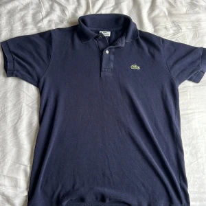 Lacoste polo mörkblå - En fin mörkblå polo från Lacoste i perfekt skick.