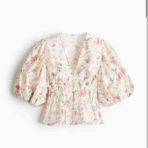 Blommig blus med puffärm och v-ringning - Supersöt blommig blus i vitt. Blusen har v-ringning, smockad midja och puffiga trekvartsärmar. Materialet känns lätt och luftigt.