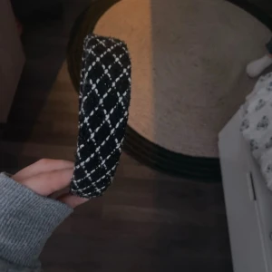 Svart diadem med rutigt mönster - Snyggt svart diadem med vitt rutmönster. Diademet är vadderat och har en mjuk textil på utsidan som ger en lyxig känsla. Perfekt accessoar för att lyfta din look och hålla håret på plats.