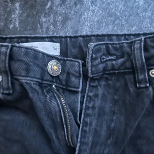 Svarta jeansbyxor i rak modell barn - Säljer ett par svarta jeansbyxor i klassisk rak modell med dragkedja och knapp framtill. Byxorna har fem fickor och bälteshällor, perfekta till sneakers eller boots. Materialet är slitstarkt jeans och färgen är mörk svart.