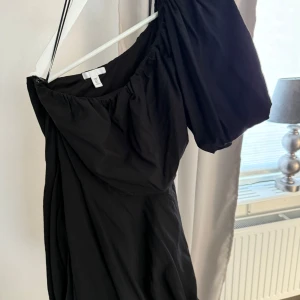 Svart oneshoulder klänning - Snygg svart oneshoulder klänning från H&M. Perfekt för en kväll ute eller en speciell tillställning. Klänningen har en elegant design med en axel och en lös passform som ger en stilren look.