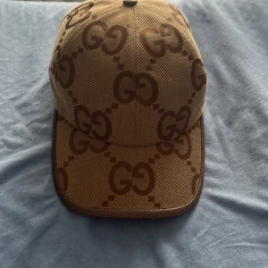 Beige och brun keps från Gucci - Snygg keps från Gucci i beige och brunt med det ikoniska GG-mönstret. Perfekt för att ge din outfit en lyxig touch. Kepsen har en klassisk design med böjd skärm och justerbar passform.