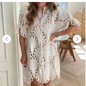 Vit spetsklänning - Säljer en vacker vit spetsklänning med korta ärmar och detaljerad brodering. Klänningen har en luftig passform och knappar framtill. Perfekt sommaren och som studentklänning