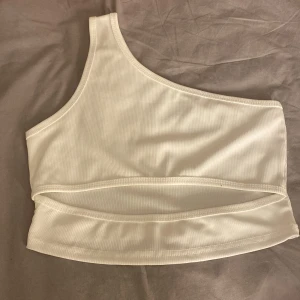 Vit ribbad oneshoulder topp - Snygg vit ribbad oneshoulder topp som är perfekt för en stilren look. Den har en unik asymmetrisk design och är tillverkad i ett mjukt material som ger en bekväm passform. Perfekt för att lyfta vilken outfit som helst!