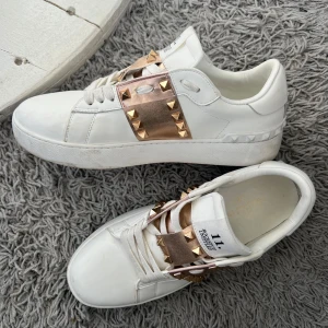 Valentino Garavani - Vita Valentino Gatavani med guldiga nitar och band över snörningen. Perfekta för att ge en lyxig touch till din outfit. Skorna har en rund tå och är tillverkade i skinn. Storleken är 38 men passar även 37 💕Ancönt dessa typ 2 gånger, smutsen går enkelt att tvätta bort med varm trasa. 