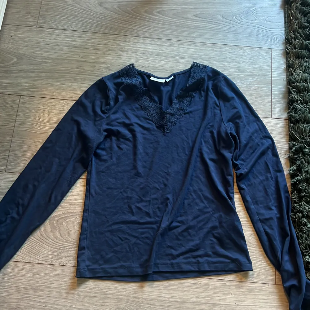 Säljer en stilren svart långärmad topp från Gina Tricot med spetsdetaljer vid halsringningen. Perfekt för en elegant look. . Neuletakit & Villapaidat.