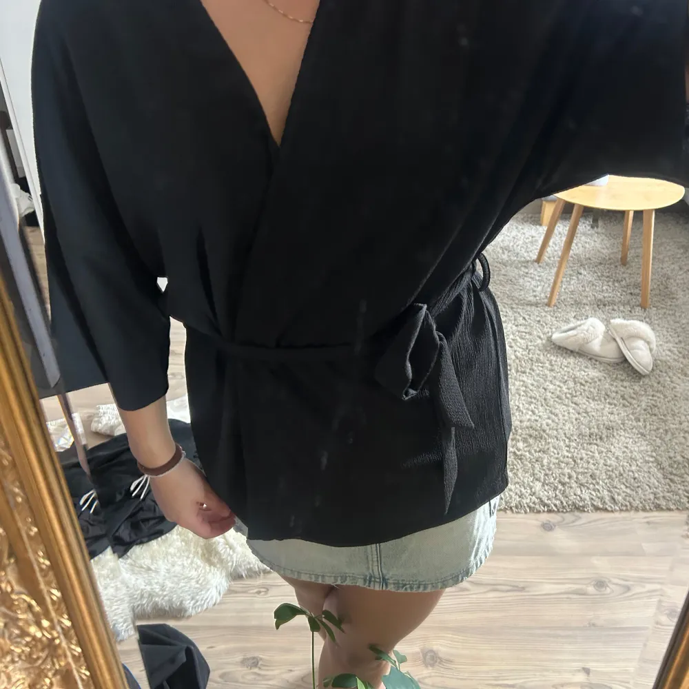 Snygg svart omlottblus med trekvartsärmar och knytband i midjan. Perfekt för en stilren look. Blusen har en lös passform och är tillverkad i ett mjukt material.. Puserot.