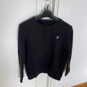 Svart sweatshirt från Lyle & Scott - Säljer en stilren svart sweatshirt från Lyle & Scott med deras ikoniska logga på bröstet. Tröjan har långa ärmar och en rund halsringning. Perfekt för en avslappnad look.