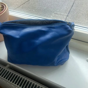 Blå pouch med mönstrat foder - Snygg blå pouch, pouchbag, väska, necessär i skinn med ett mönstrat. Väskan har en praktisk dragkedja upptill för säker förvaring av dina saker. Perfekt för att ge en färgklick till din outfit.