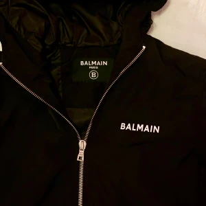 Svart jacka från Balmain Paris  - Snygg svart jacka från Balmain Paris med dragkedja och vit logotyp på bröstet och ryggen. Perfekt för en stilren look.