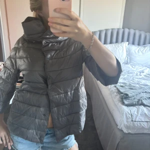 Grå dunjacka med trekvartsärm - Sjukt snygg trekvartärmad Henro liknande jacka som aldrig är andvänd i grå/beige nyans!Snygg grå dunjacka med trekvartsärm och hög krage. Jackan har en stilren design med dragkedja och knappar framtill. Perfekt för kyligare dagar när du vill hålla stilen.