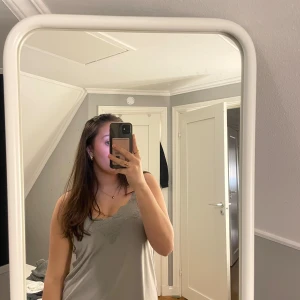 Grå linnetopp från Amisu - Säljer en stilren grå linnetopp från Amisu med spetsdetaljer vid halsringningen. Toppen har smala axelband och en v-ringad design som ger en elegant touch. Perfekt för att lägga till en feminin känsla till din outfit.