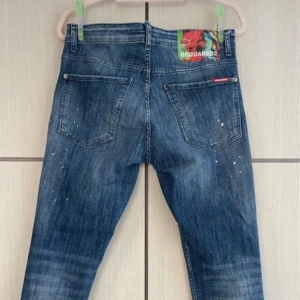 Blå jeans från Dsquared2 - Snygga blå jeans från Dsquared2 med en cool slitningseffekt och vita färgstänk. De har en klassisk femficksdesign och knappgylf. Perfekta för en avslappnad stil.