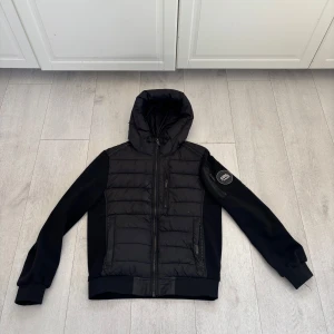 Svart jacka med huva från Supply & Demand - Snygg svart jacka från Supply & Demand med huva och dragkedja. Jackan har en quiltad design på framsidan och en praktisk ficka med dragkedja på ärmen. Perfekt nu till våren. Den är i storlek S ny pris 1100kr priset kan diskuteras vid snabb affär 