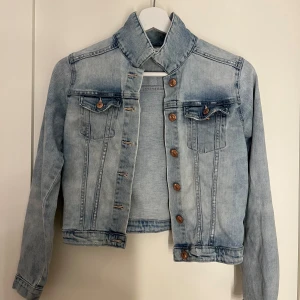 Ljusblå jeansjacka från H&M - Snygg ljusblå jeansjacka från H&M med knappar i bronsfärg. Jackan har två bröstfickor med knapp och en klassisk krage. Perfekt för vår och sommar!