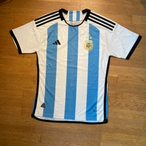 Adidas Argentina 2023 football tröja  - Säljer en snygg Argentina 2023 med autenticitet fotbollströja från Adidas i vitt och blått. Tröjan har korta ärmar och är tillverkad med Parley Ocean Plastic. Perfekt för fotbollsfans!