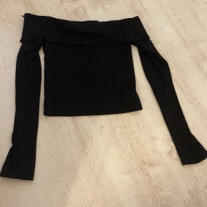 Svart offshoulder topp från H&M Divided - Snygg svart offshoulder topp från H&M Divided i ribbat material. Perfekt för en stilren look med långa ärmar och en tight passform. Passar utmärkt till både jeans och kjol.
