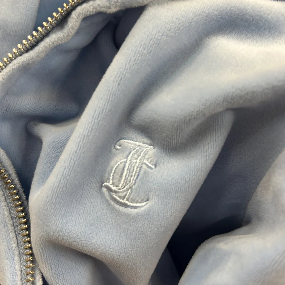 Säljer en ljusblå hoodie från Juicy Couture med dragkedja och huva. Perfekt för en avslappnad stil. Den har långa ärmar och en mjuk känsla.. Neuletakit & Villapaidat.
