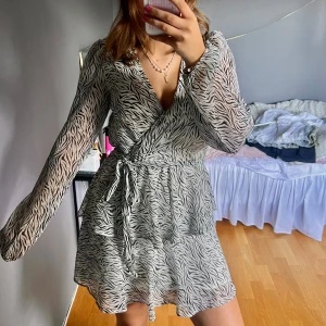 Zebramönstrad klänning  - Snygg zebramönstrad klänning med v-ringning och långa ärmar. Klänningen har ett knytband i midjan.