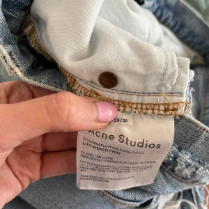 Ljusblå jeans från Acne Studios - Snygga ljusblå jeans från Acne Studios med fransiga detaljer vid bensluten och slitningar vid fickorna. De har en klassisk femficksdesign och knappgylf. Perfekta för en avslappnad stil.